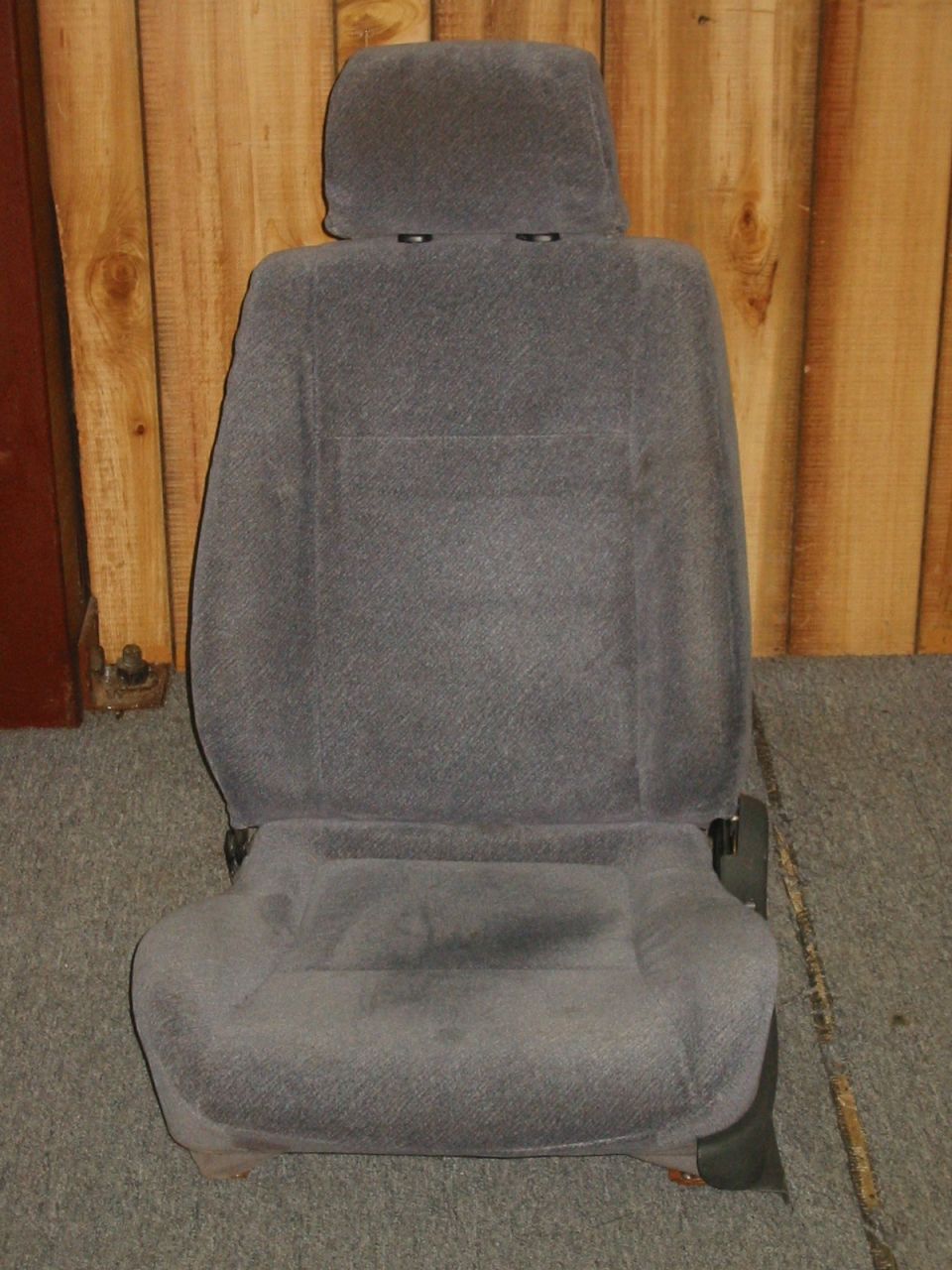 Gray cloth bucket seat with headrest removed from vehicle, photographed against wood paneling
