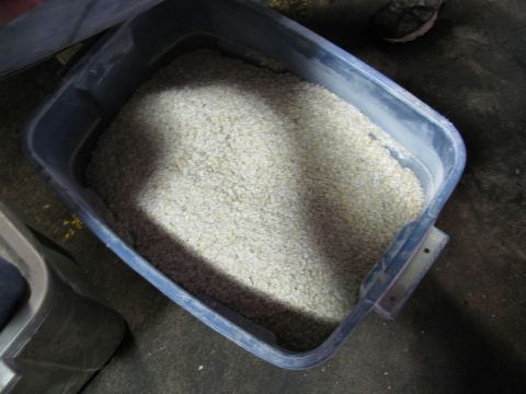 1985 Ford LTD Crown Victoria - A large plastic bin is filled with grain. The bin is dark blue and sits on a dark floor.