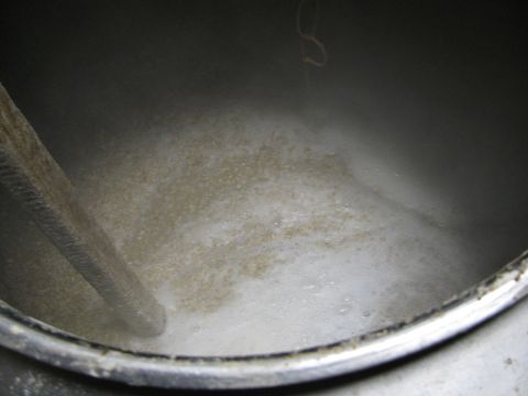 1985 Ford LTD Crown Victoria - A close-up view inside a large metal vat shows a brewing mash with foam and a wooden paddle, indicating a process of making beverages.