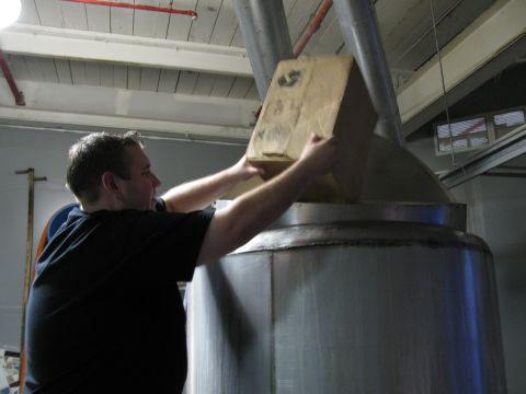 1985 Ford LTD Crown Victoria - A man is shown adding ingredients to a large industrial vat during a brewing process.