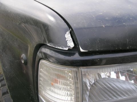 1996 Ford Bronco - Close-up of a black SUV's fender showing damage and a clear headlight.