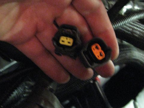 1994 Ford Probe - Two electrical connectors are held in a hand, one yellow and one orange, with engine components in the background.