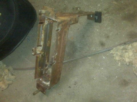 1995 Ford Bronco - This is a rusted metal bracket, likely a vehicle part, on a concrete floor.