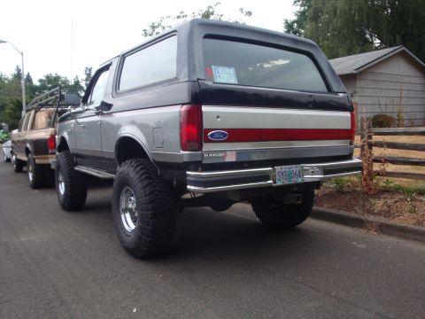 1989 Ford Bronco - A lifted 1989 Ford Bronco is parked on a street, with another vehicle behind it.