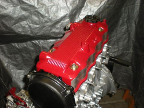 Suzuki Samurai - A red engine valve cover is shown mounted on a silver engine block, against a dark, textured background.