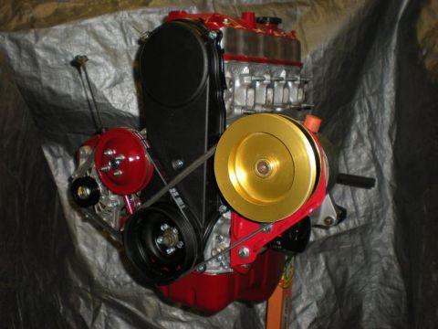Suzuki Samurai - Front accessory-drive end of a freshly assembled four-cylinder engine standing on a stand against a gray tarp, painted red with a bare alum…