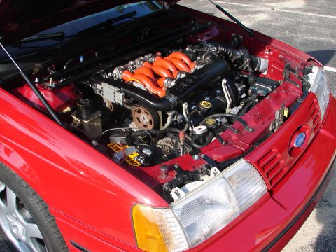 1992 Ford Taurus - The engine bay of a red 1992 Ford Taurus is visible with the hood open, revealing the V8 engine.