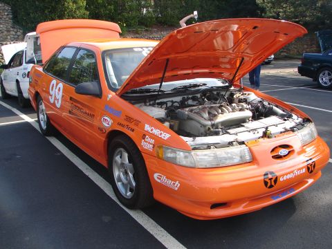 1992 Ford Taurus - Orange 1992 Ford Taurus race car with hood open, parked next to another vehicle.