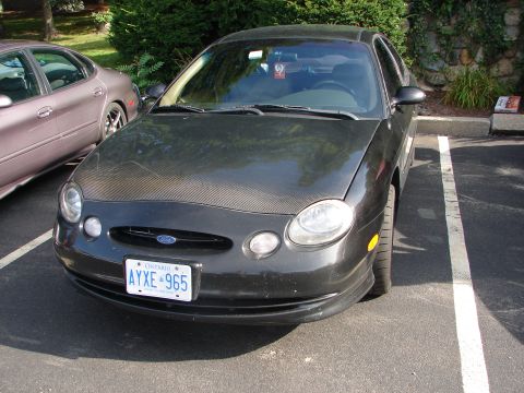 1992 Ford Taurus - This dark gray sedan, identified as a Ford Taurus, is parked in a lot with another vehicle. The hood appears to be a carbon fiber wrap.