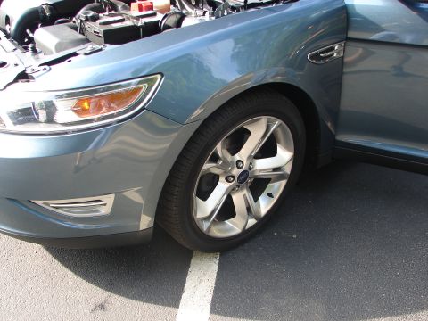 1992 Ford Taurus - Front fender and wheel of a blue sedan, likely a Ford Taurus from the 2010 model year, with the hood open.