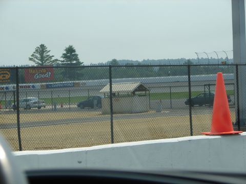 1992 Ford Taurus - Several cars are visible on a racetrack, viewed through a chain-link fence.