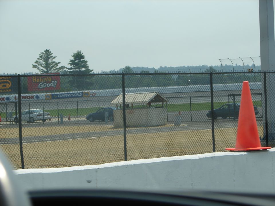 Cars on a racetrack behind a fence with an orange cone in the foreground