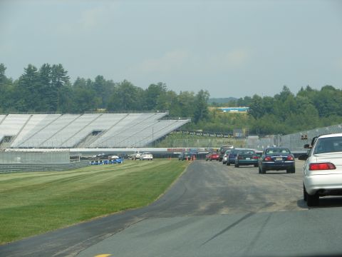 1992 Ford Taurus - Multiple vehicles are parked on the asphalt near a racetrack and grandstands.
