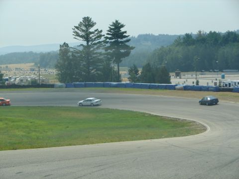 1992 Ford Taurus - Several cars are on a race track, with trees and RVs visible in the distance.