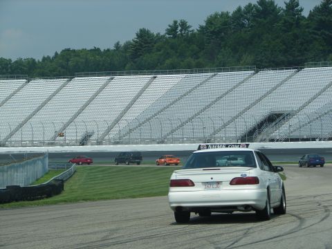 1992 Ford Taurus - A white 1992 Ford Taurus sedan drives on a race track with empty grandstands in the background.