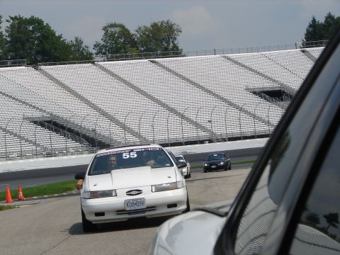 1992 Ford Taurus - A white 1992 Ford Taurus with racing number 55 drives on a track in front of stadium seating.