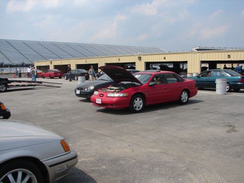 1992 Ford Taurus - A red 1992 Ford Taurus is parked with its hood up at a racing event.
