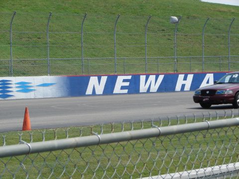1992 Ford Taurus - A maroon sedan is seen on a race track, with a partial 'NEW HA' mural on the wall behind it.