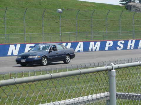 1992 Ford Taurus - A dark blue 1992 Ford Taurus sedan drives on a race track with a "NEW HAMPSHIRE" banner in the background.