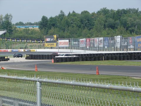 1992 Ford Taurus - Cars race on a track with numerous sponsor advertisements and tire barriers lining the course.