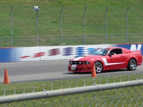 1992 Ford Taurus - A red Ford Mustang with white racing stripes drives on a track with orange cones.