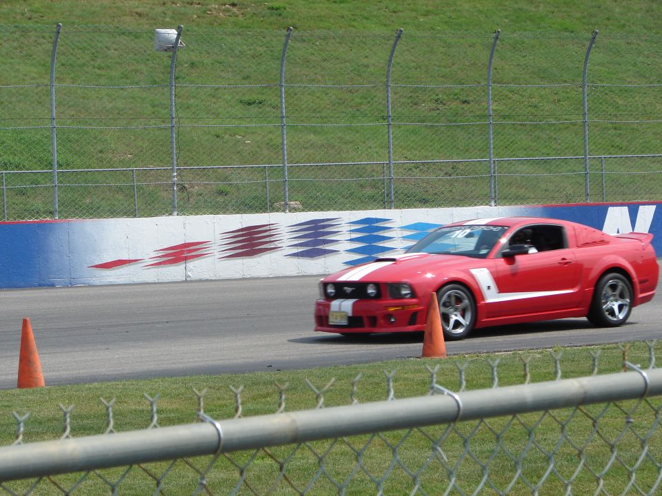 Red Ford Mustang with white stripes on a race track, cones on the side