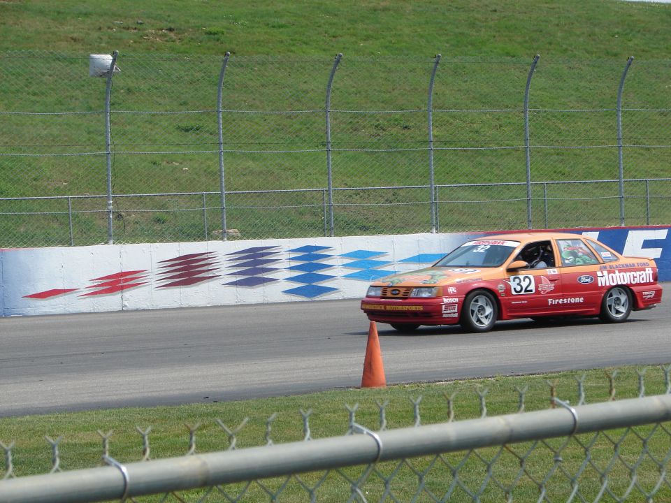 Red and orange racing sedan with number 32 on door, driving on a track. Motorcraft and Firestone decals visible