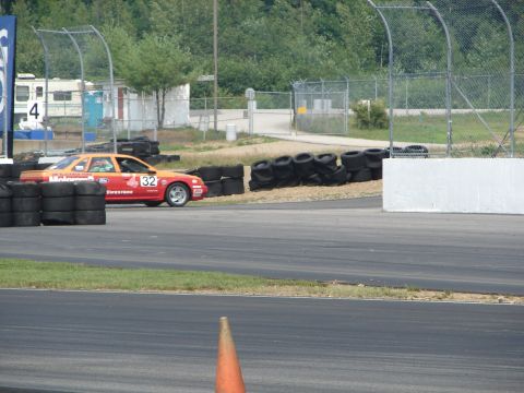 1992 Ford Taurus - A race car with sponsor decals and the number 32 navigates a turn on a race track.