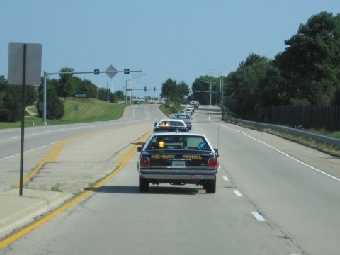 1991 Ford Crown Victoria - A line of highway patrol cars drives down a road on a clear day.