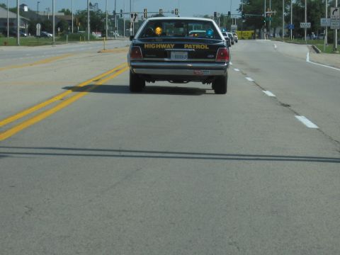 1991 Ford Crown Victoria - A 1991 Ford Crown Victoria highway patrol car is seen from behind on a road with other vehicles in the distance.