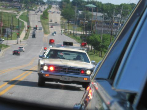 1991 Ford Crown Victoria - A vintage police car with flashing red lights drives down a suburban street.