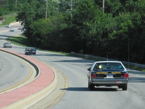 1991 Ford Crown Victoria - A highway patrol car is seen from behind on a road with trees lining the side.