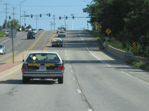 1991 Ford Crown Victoria - A 1991 Ford Crown Victoria, marked as a highway patrol vehicle, drives on a sunny day with other cars on the road.