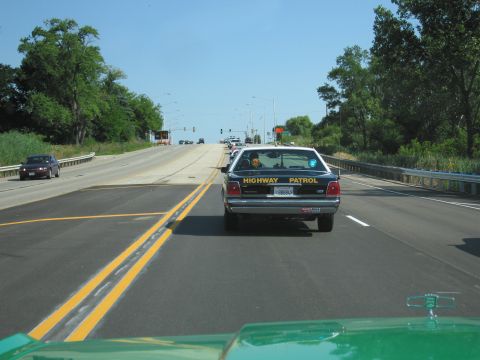 1991 Ford Crown Victoria - A highway patrol car is driving on a sunny day on a multi-lane road.
