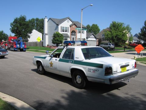 1991 Ford Crown Victoria - A police car is parked on a residential street, with a tow truck visible in the distance.