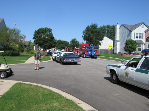 1991 Ford Crown Victoria - A 1991 Ford Crown Victoria police car is seen from the rear, parked on a suburban street with tow trucks in the background.