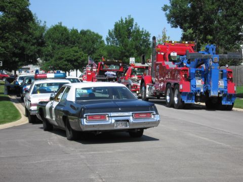 1991 Ford Crown Victoria - A line of police cars and tow trucks are parked on a street on a sunny day.