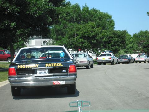 1991 Ford Crown Victoria - A line of highway patrol cars, including a 1991 Ford Crown Victoria, are parked on a residential street.