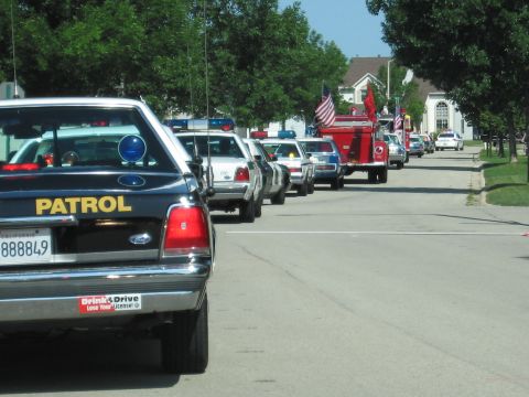 1991 Ford Crown Victoria - A line of police cars and a fire truck drive down a suburban street during a parade.