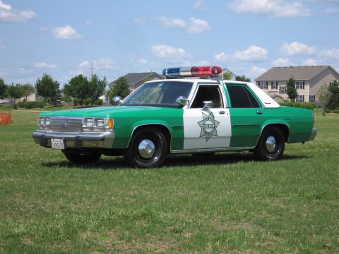1991 Ford Crown Victoria - This vintage sheriff's car, likely from the 1980s, features a distinctive green and white paint scheme and a star badge on the door.