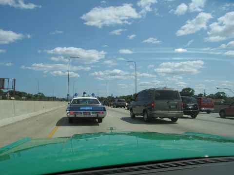 1991 Ford Crown Victoria - A police car is seen from behind on a busy highway under a cloudy sky.