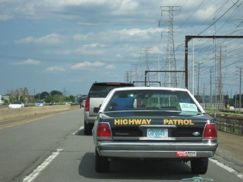 1991 Ford Crown Victoria - A black 1991 Ford Crown Victoria police car is seen from behind on a highway, with power lines overhead.