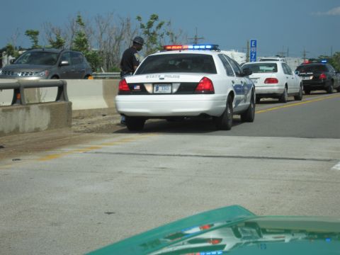 1991 Ford Crown Victoria - A state police vehicle is stopped on the highway, with other cars in traffic behind it.