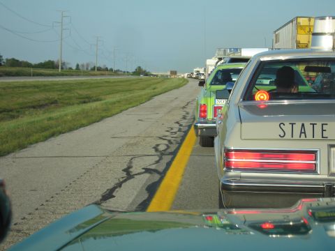1991 Ford Crown Victoria - A line of cars are stuck in traffic on a highway with power lines visible in the background.