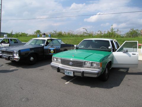1991 Ford Crown Victoria - Two police cars, a 1991 Ford Crown Victoria and an older model, are parked side-by-side on asphalt.