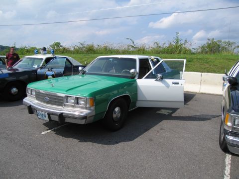 1991 Ford Crown Victoria - Two police cars are parked side-by-side, one with its front doors open.
