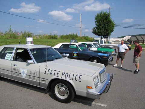 1991 Ford Crown Victoria - Several police cars, including a light-colored sedan and a dark blue sedan, are parked in a lot on a sunny day.