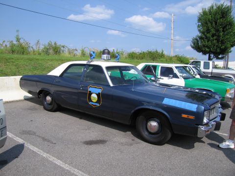 1991 Ford Crown Victoria - This police car, likely a 1977 model, is parked in a lot with other vehicles under a clear blue sky.