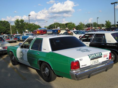 1991 Ford Crown Victoria - Sheriff's car, possibly a 1991 Ford Crown Victoria, parked with other vehicles under a cloudy sky.