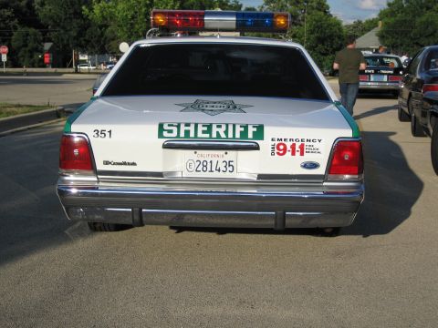 1991 Ford Crown Victoria - A 1991 Ford Crown Victoria police car is seen from the rear, parked on a street with other vehicles nearby.